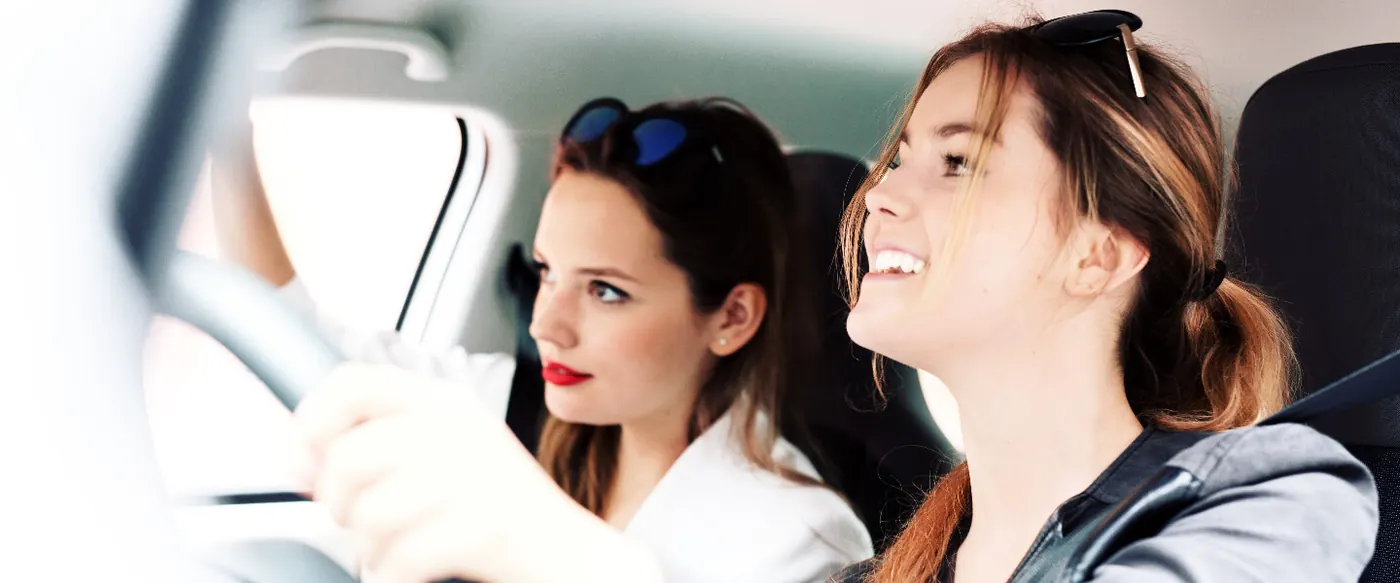 Zwei junge Frauen sitzen lachend im Auto